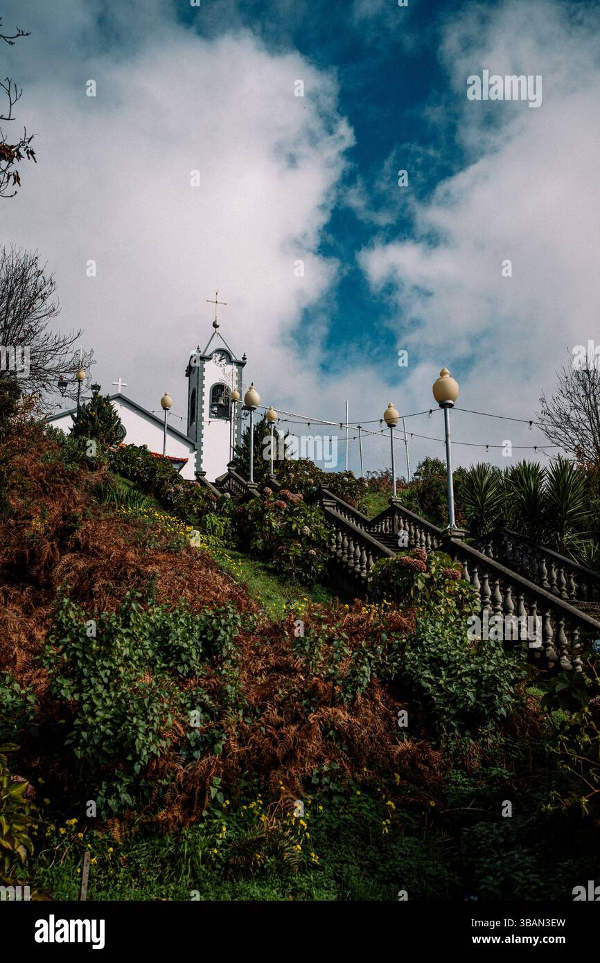 Weiße Kirche mit Glockenturm auf einem üppig grünen Hügel mit kunstvoller Steintreppe Stockfoto
