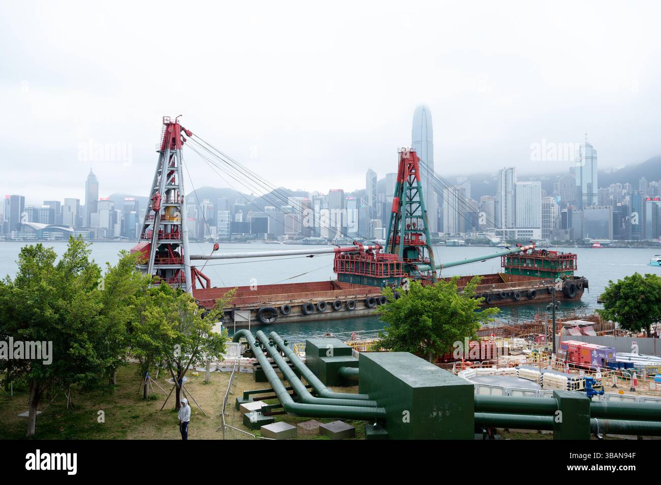 Schwimmende Krankähne im Victoria Harbour, hinter der sich die nebelummantelte Skyline von Hong Kong Island erhebt Stockfoto