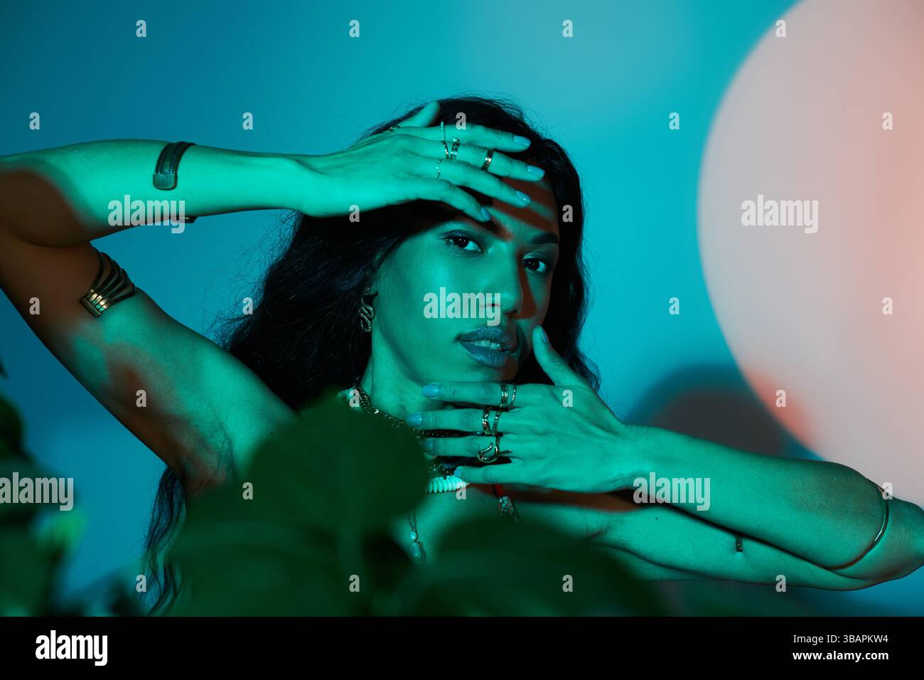 Anmutige junge Frau posiert inmitten üppiger Pflanzen und künstlerischer Schatten im Sommerstil. Stockfoto