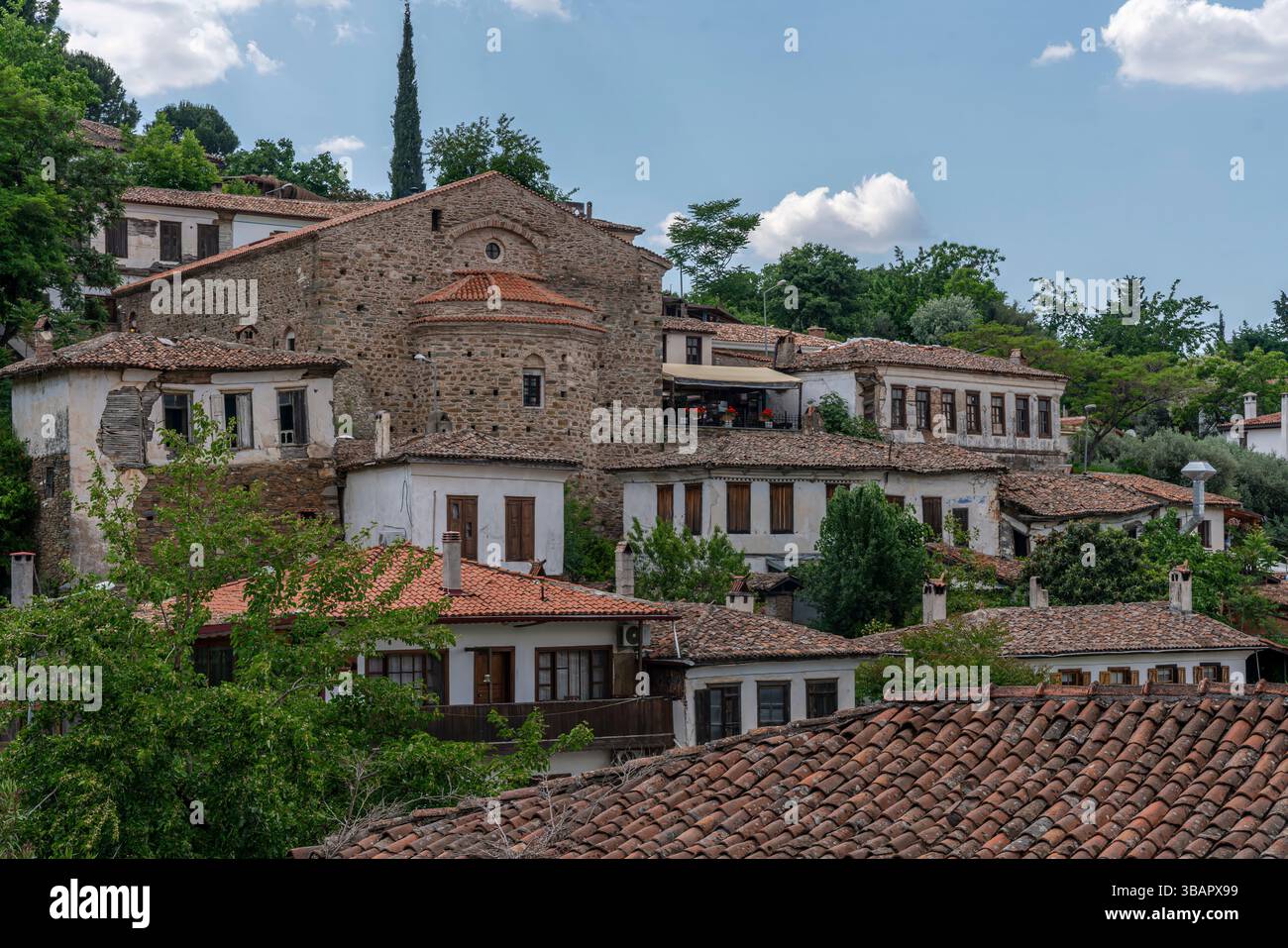 In Sirince steht die Kirche St. Johannes des Täufers zwischen weißen Häusern und üppigen Bäumen und verbindet christliches Erbe mit türkischer Dorflandschaft. Stockfoto