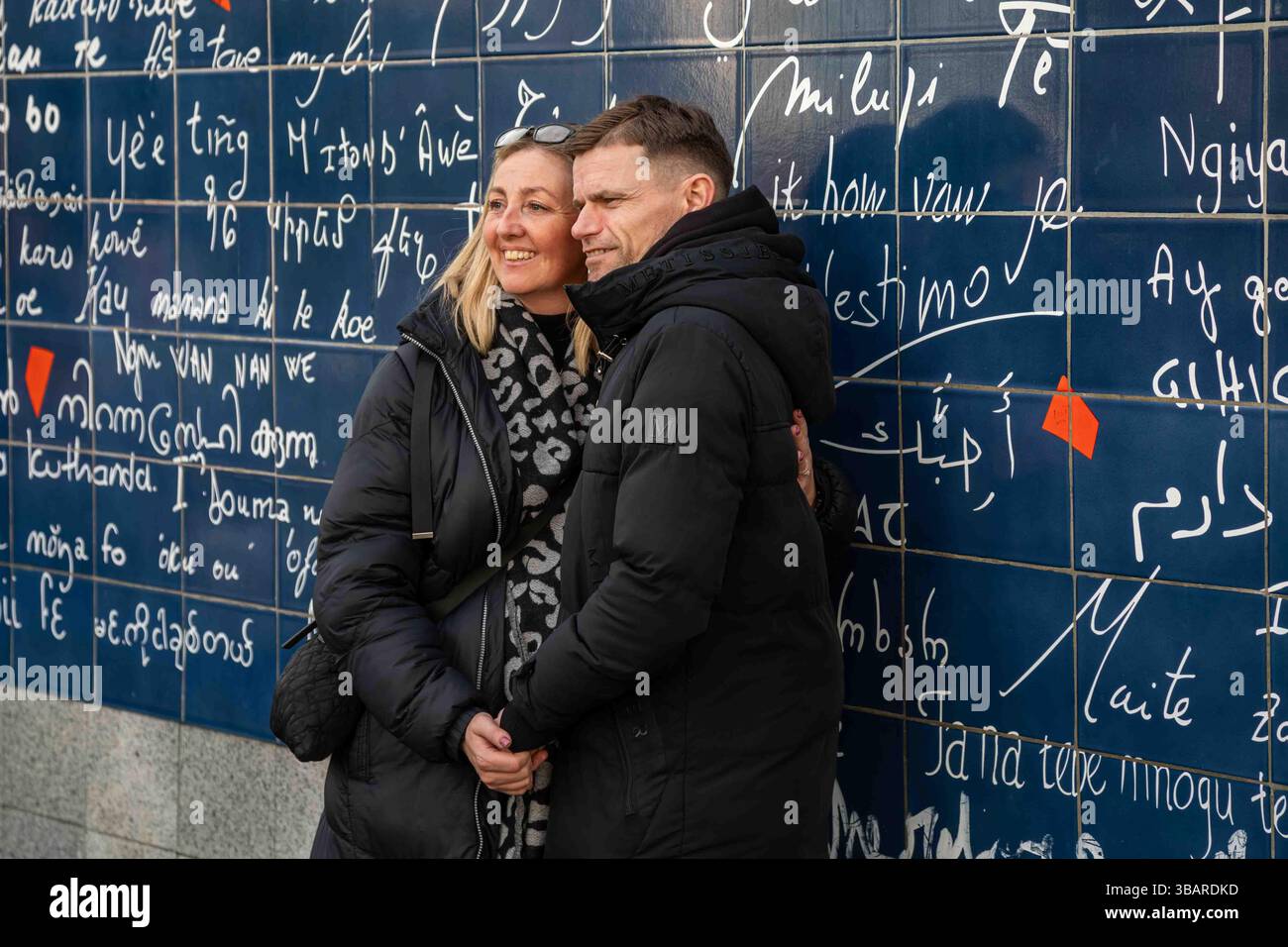 Touristen-Paar posiert gegen Le Mur des je Taime oder Wall of I Love You auf dem Square Jehan Rictus in Montmartre in Paris, Frankreich Stockfoto
