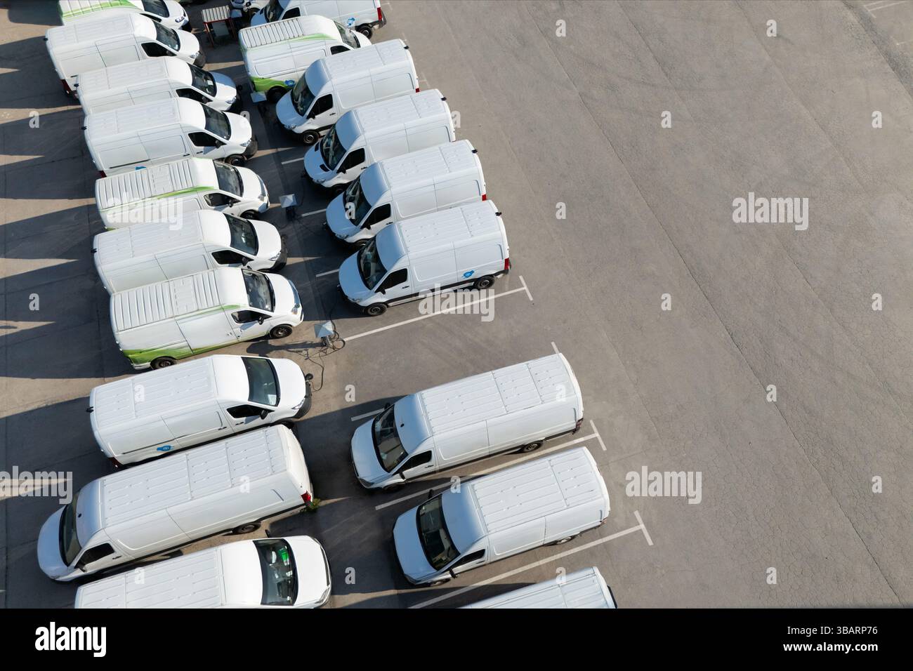 Reihen weißer Elektrotransporter an Ladestationen für Elektrofahrzeuge. Stockfoto