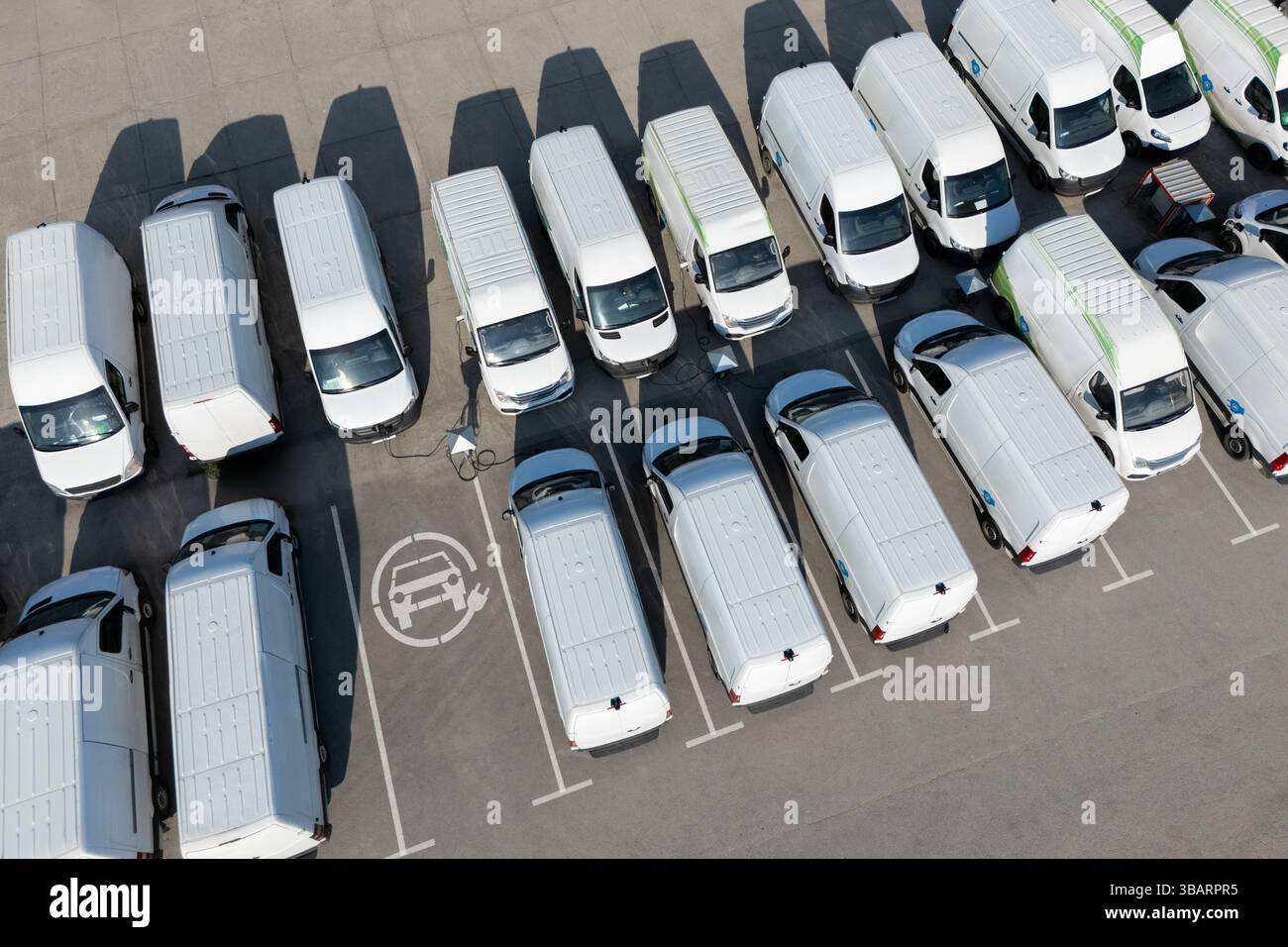 Reihen weißer Elektrotransporter an Ladestationen für Elektrofahrzeuge. Stockfoto