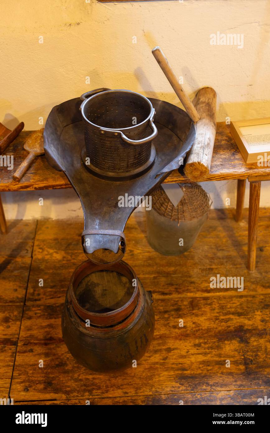 Vintage-Metallsieb mit Griffen, die in Holzeimer auf Holztisch mit Werkzeugen und Demijohn abfließen Stockfoto