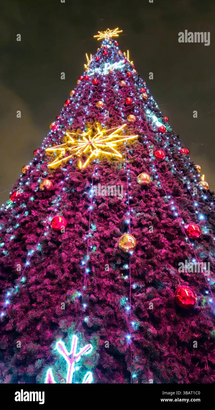 Großer Weihnachtsbaum, dekoriert mit großen glühenden Schneeflocken, Girlanden und bunten Kugeln vor dem Nachthimmel, Blick von unten Stockfoto