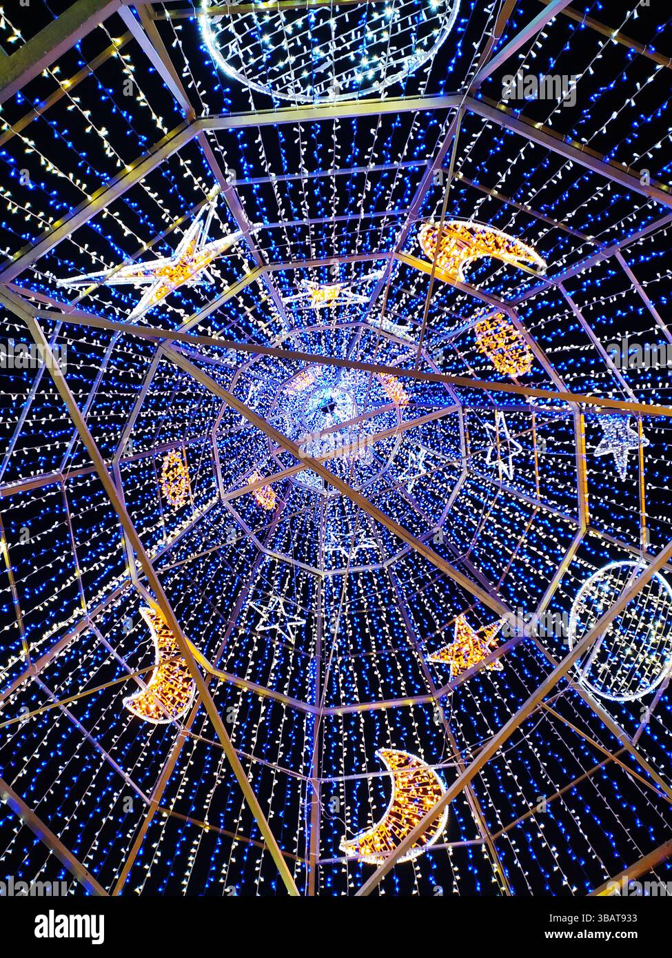 Atemberaubender Flachwinkelblick einer blendenden Lichtinstallation. Blaue und warmweiße LED-Leuchten zieren einen geometrischen Rahmen und erzeugen Sterne und Halbmond Stockfoto
