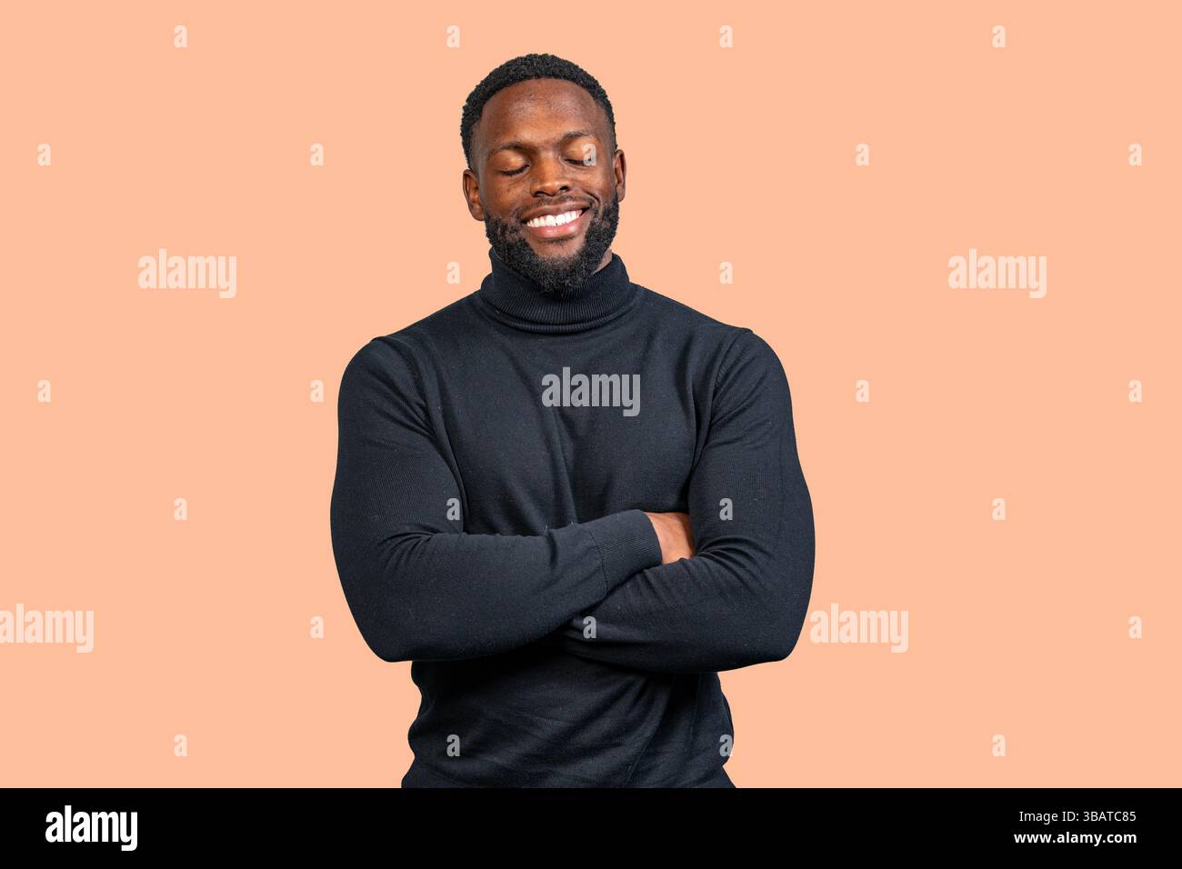 Studio-Porträt eines lächelnden Geschäftsmannes, der einen schwarzen Rollkragenpullover trägt, mit gefalteten Armen und geschlossenen Augen vor einem braunen Hintergrund steht Stockfoto