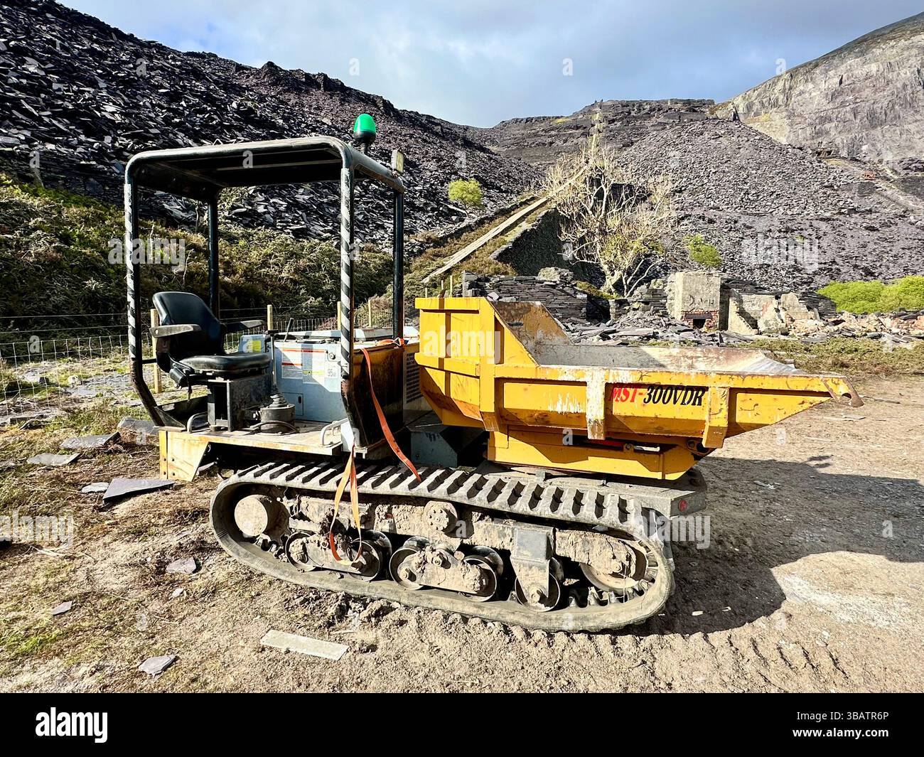 Raupenkipper im Dinorwic Quarry in der Nähe von Llanberis, Nordwales, mit einem Hintergrund aus Schiefer und dramatischer Steinbruchlandschaft unter bewölktem Himmel. - Smartphone-aufgenommenes Stockfoto