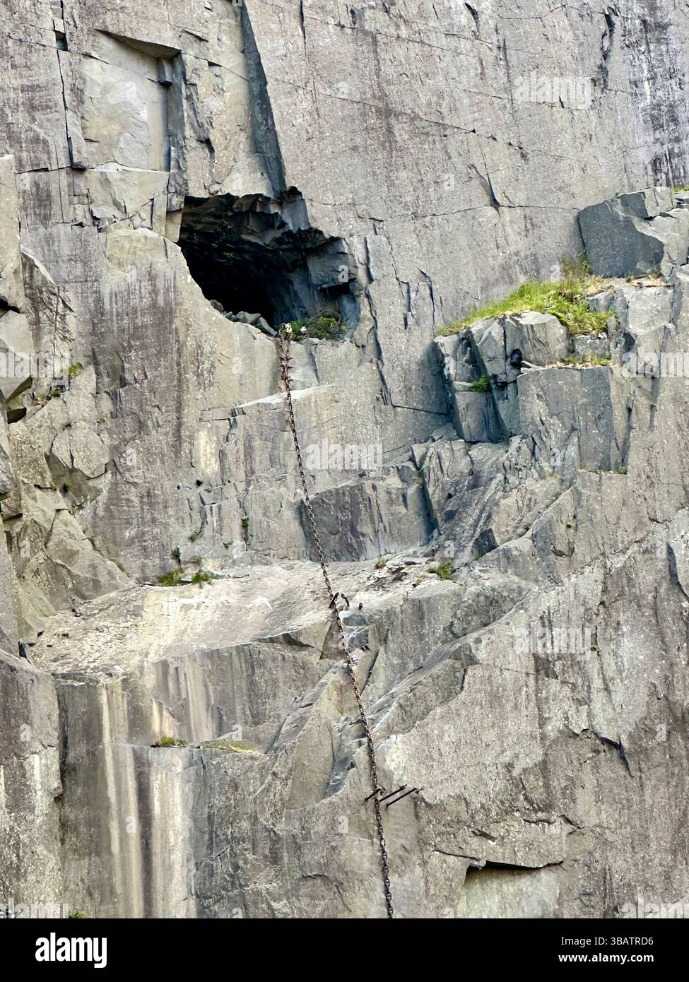 In Stein gehauene Stufen und ein großes Loch mit einer Kette, die in das Loch hineinführt, im Dinorwic Quarry in Wales zu sehen. Historische Industriestandorte. - Smartphone-aufgenommenes Stockfoto