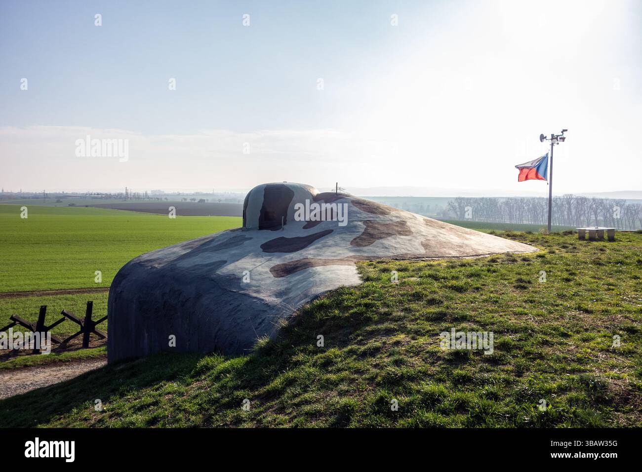 Kriegsbunkerdenkmal in Milostovice in der Nähe von Opava mit einer Igelbarriere aus Metall im Hintergrund und schwenkender tschechischer Flagge Stockfoto