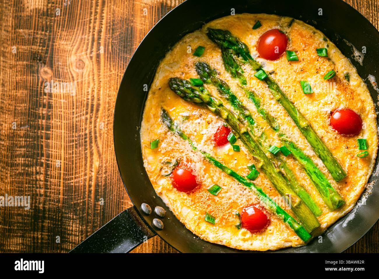 Spargel mit Rührei und Kirschtomaten in einer Pfanne auf hölzernem Hintergrund. Blick von oben. Leerzeichen für Text. Hochwertige Fotos Stockfoto