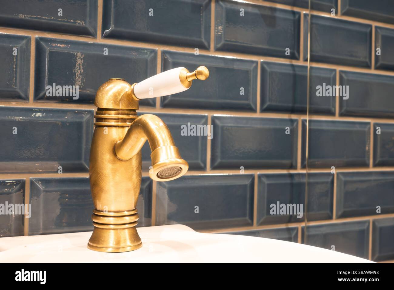 Nahaufnahme eines bunten blauen Badezimmerkonzepts mit dunkelblauen Fliesen und einem Messinghahn im antiken Stil und Wasserhahn auf einem weißen Waschbecken Stockfoto