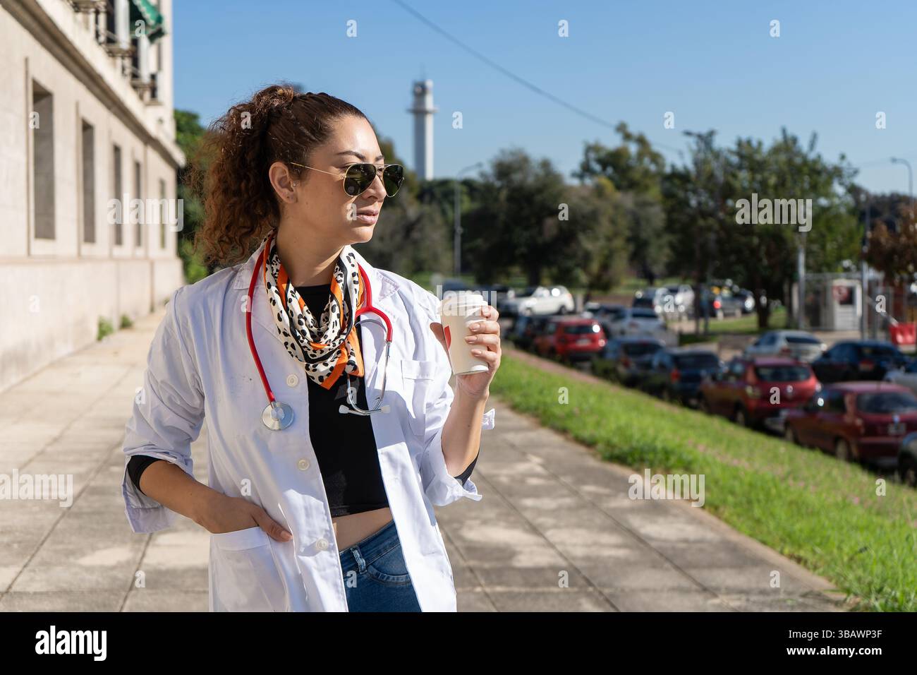 Ein selbstbewusster Arzt genießt einen Kaffee zum Mitnehmen außerhalb des Krankenhauses und blickt von der Kamera weg Stockfoto