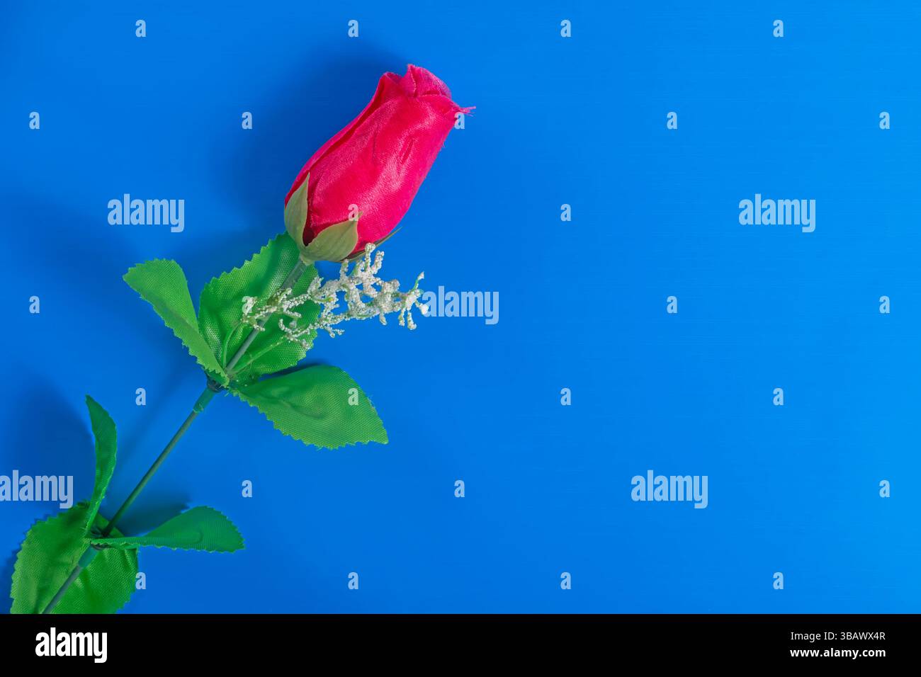 Blick von oben auf die rosa künstliche Rose mit grünen Blättern und einem blauen Hintergrund symbolisiert Romantik und Eleganz. Stockfoto