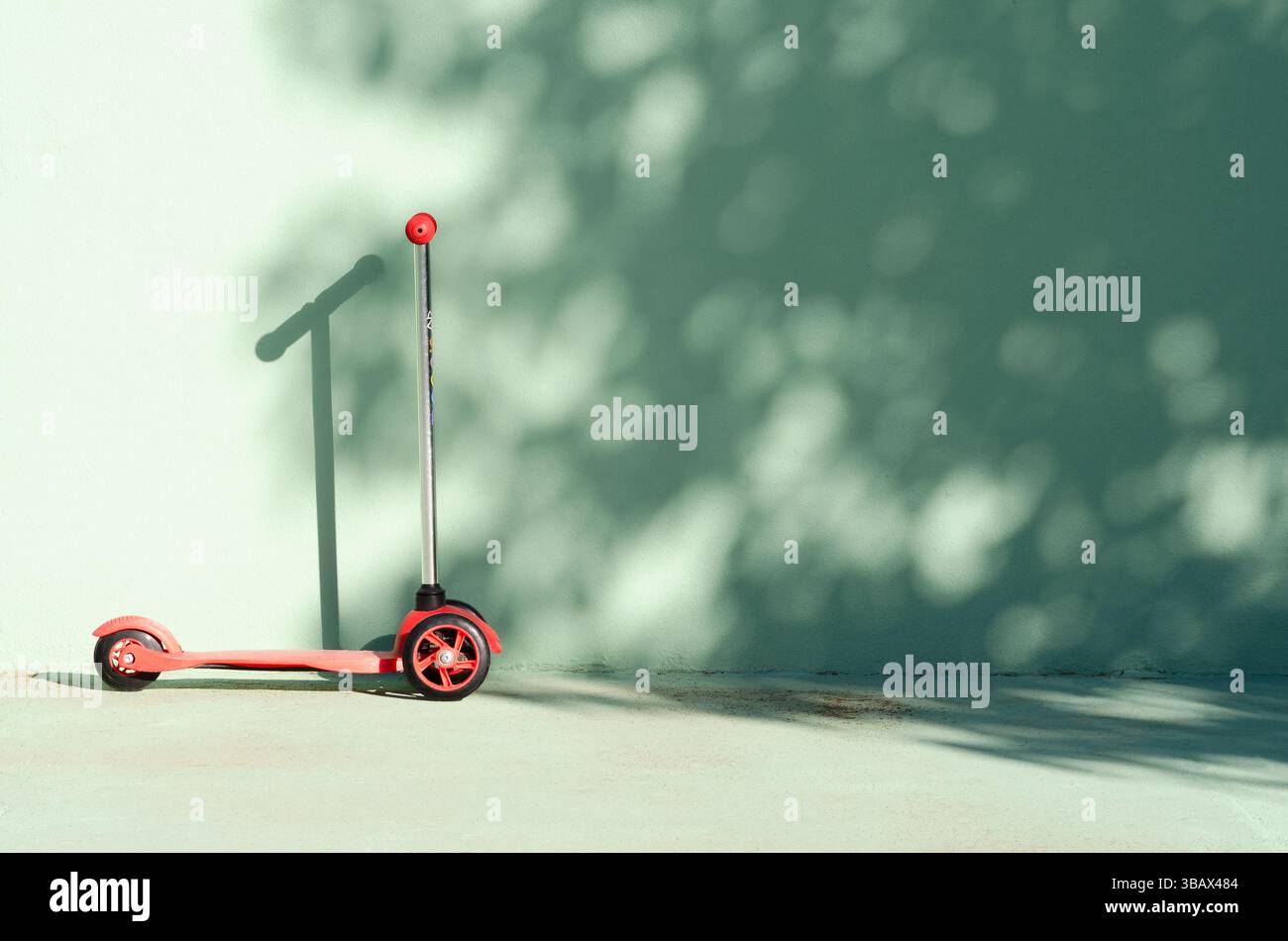 Ein Kickroller auf einer grünen Wand mit Schatten. Stockfoto