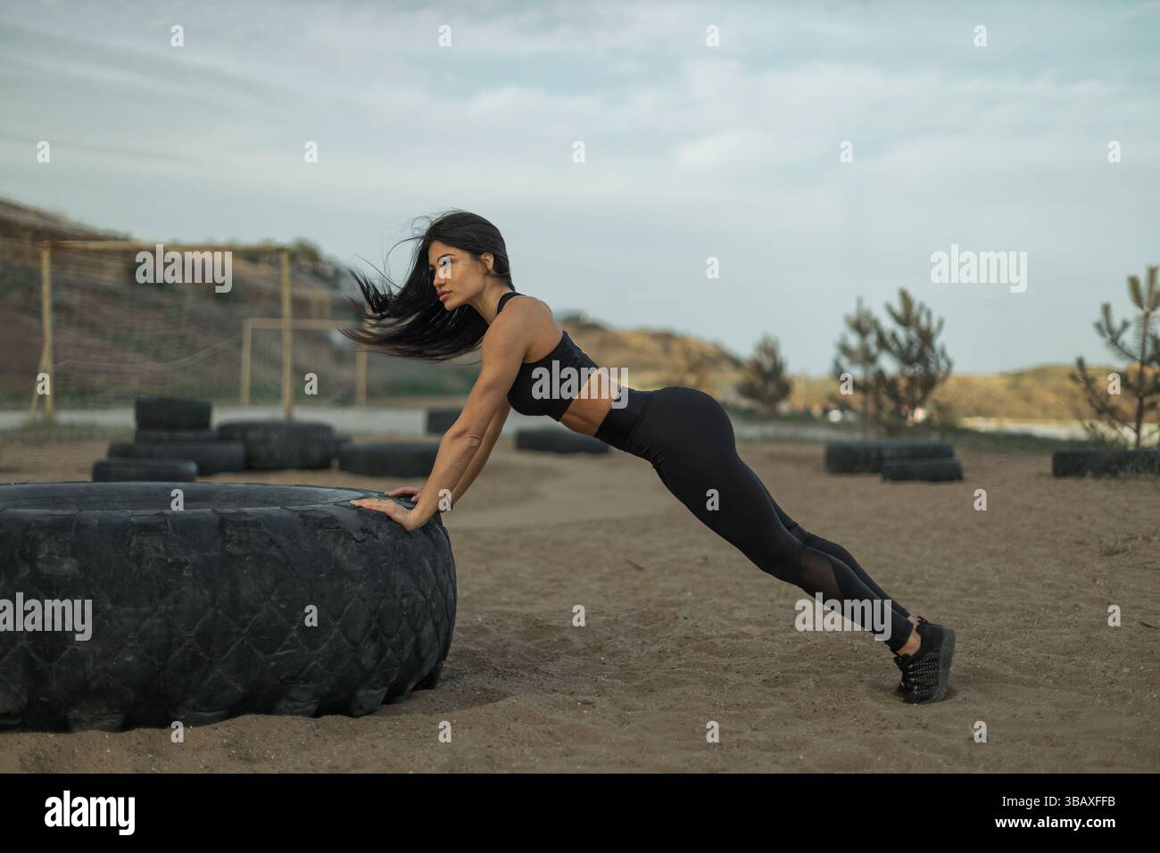 Fitnessbegeisterte nehmen an Liegestützübungen Teil, wobei sie einen großen Reifen als Stütze in einer rauen Outdoor-Umgebung verwenden. Stockfoto
