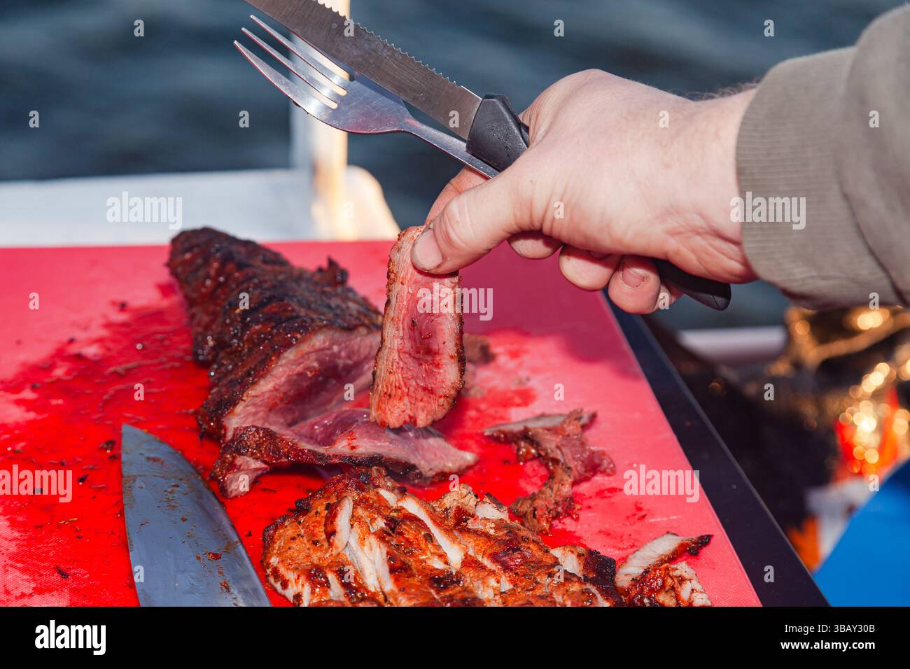 Seltenes Roastbeef Steak in Stücke geschnitten und eine menschliche Hand nimmt ein Stück. Stockfoto