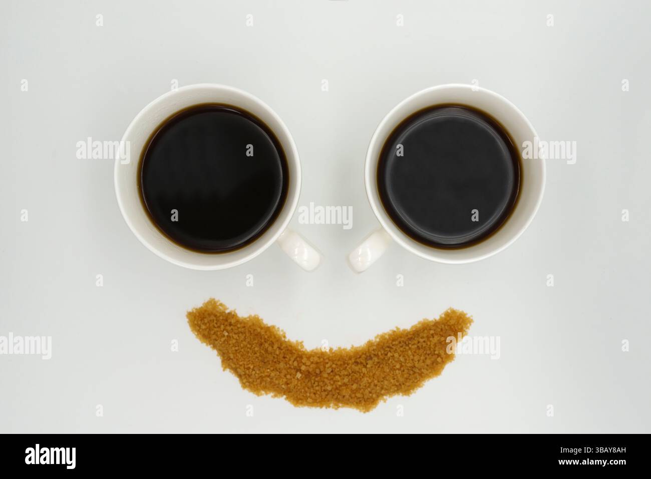 Zwei Porzellan-Kaffeetassen mit Americano und bestreuseltem Zucker in Form eines Smiley-Gesichts auf weißem Hintergrund Stockfoto