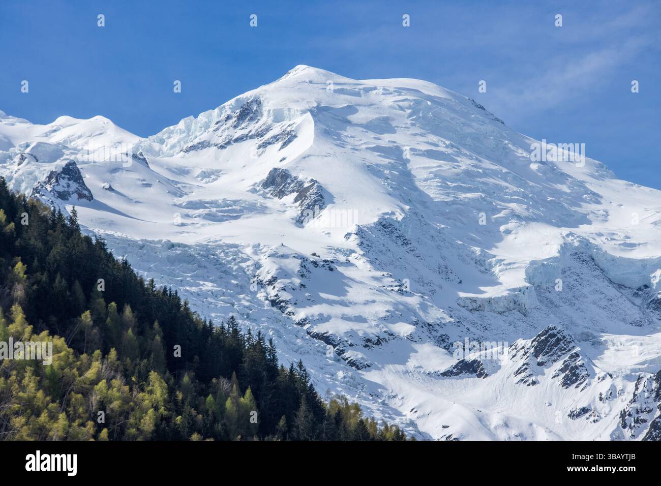 Ein wunderschöner Blick auf die Dôme du Goûter auf dem Mont Blanc-Massiv über der französischen Bergstadt Chamonix, mit Wäldern und Bäumen im Vordergrund. Stockfoto