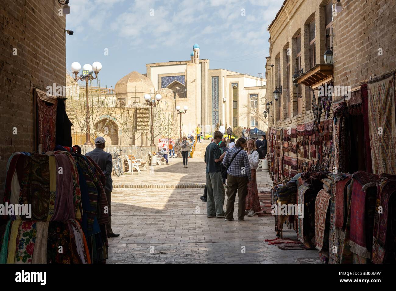 Buchara, Usbekistan - 27. März 2024: Touristen erkunden an einem sonnigen Tag einen pulsierenden Basar umgeben von historischer Architektur. Lebhafte Marktatmosphäre Stockfoto