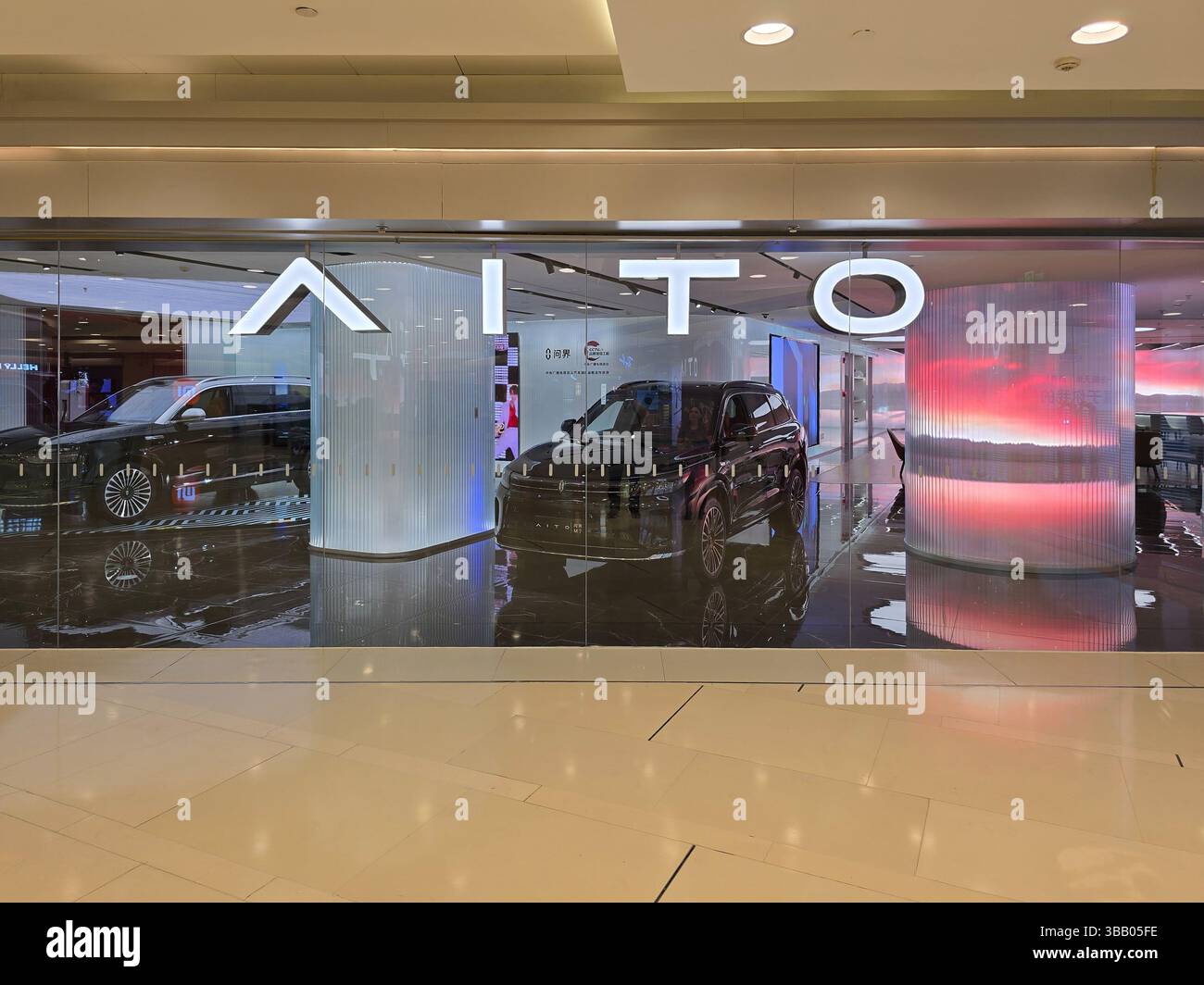 Glasfassade eines AITO Autohauses mit zwei elektrischen SUVs unter Umgebungsbeleuchtung und auffälligem Branding. Stockfoto