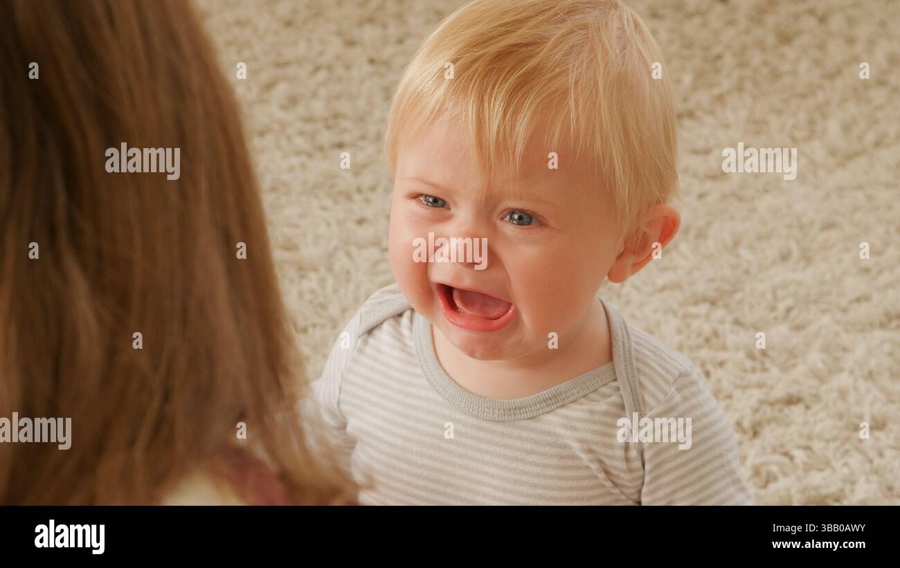 Mutter Sitzt Auf Dem Boden Der Lounge Und Tröstet Weinenden Baby-Sohn Stockfoto