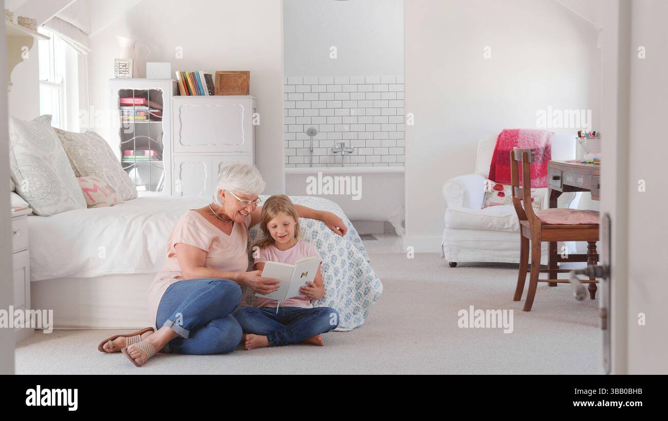Großmutter Und Enkelin Sitzen Auf Dem Boden In Einem Kühlen Schlafzimmer Und Lesen Zusammen Buch Stockfoto