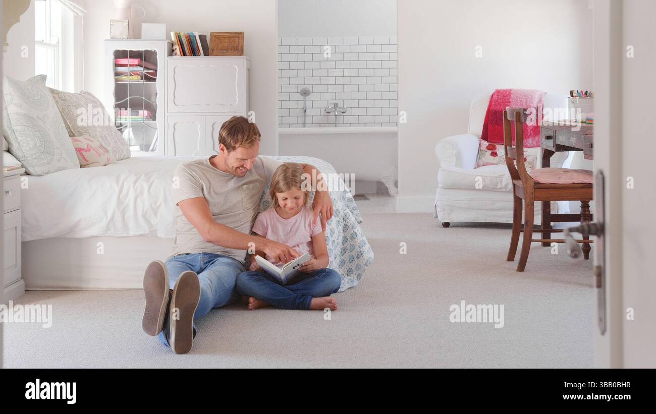 Vater Und Tochter Sitzen Auf Dem Boden In Einem Kühlen Schlafzimmer Und Lesen Zusammen Buch Stockfoto
