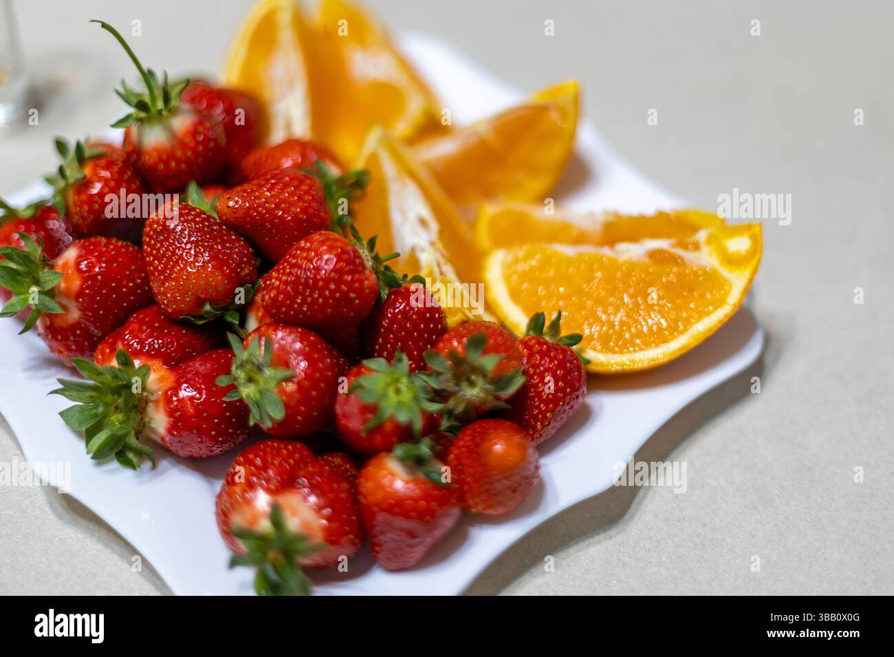 Frische Erdbeeren und Orangenscheiben auf Teller. Nahaufnahme von Reifen Erdbeeren und saftigen Orangenkeilen auf einem weißen Teller angeordnet, perfekt für gesunde Stockfoto
