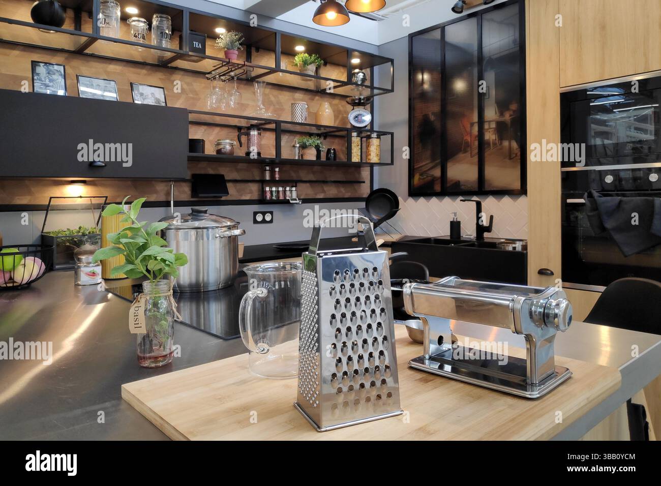 Moderne, stilvolle Küche mit industriellem Touch, mit offenen schwarzen Regalen, Edelstahlgeräten und Holzakzenten. Stockfoto