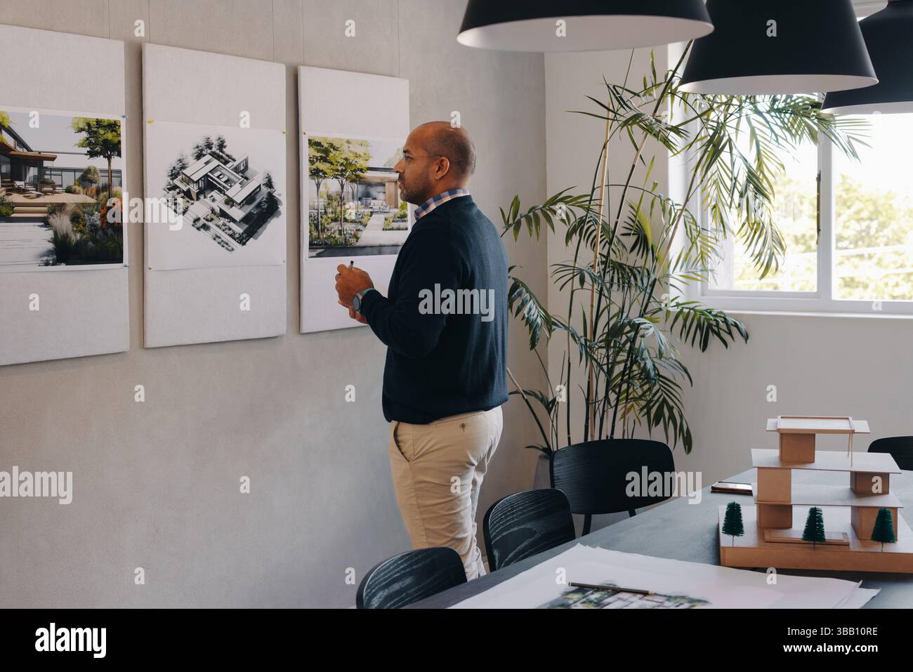 Ein Architekt untersucht Gebäudeentwürfe bei einer Projektplanungssitzung und konzentriert sich dabei auf Details und Strategien. Konzentration und Projektentwicklung in an Stockfoto