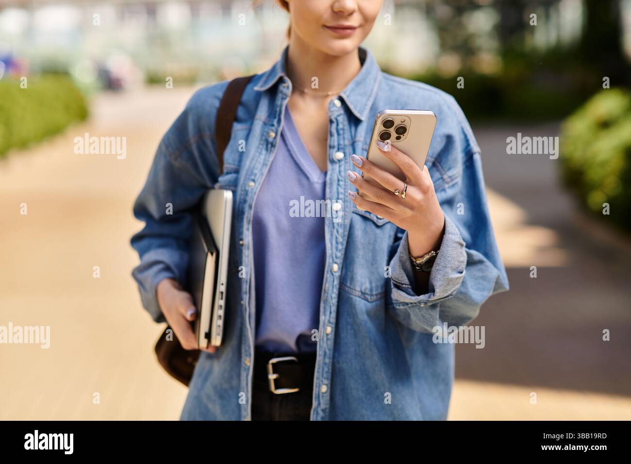 Helles Sonnenlicht hebt die rothaarige Frau hervor, wenn sie auf einem belebten Weg mit ihrem Smartphone in Berührung kommt. Stockfoto