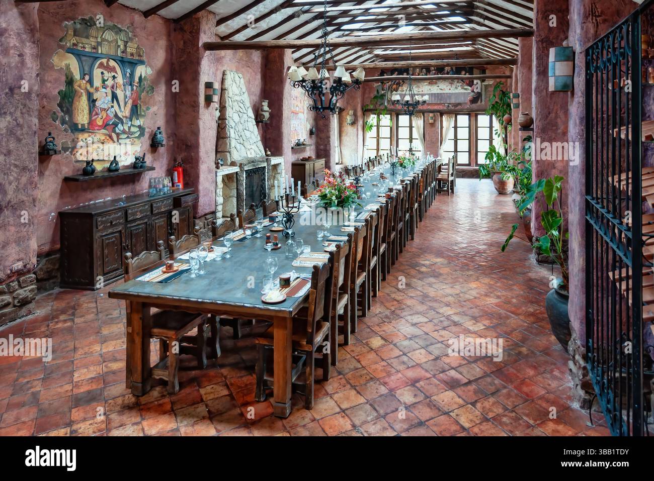 Pisac, Peru - 25. August 2010: Ein gemütlicher Speisesaal in einer peruanischen Hacienda, mit rustikalem Holztisch, antikem Dekor, lebhaften Textilien und üppigem Grün Stockfoto
