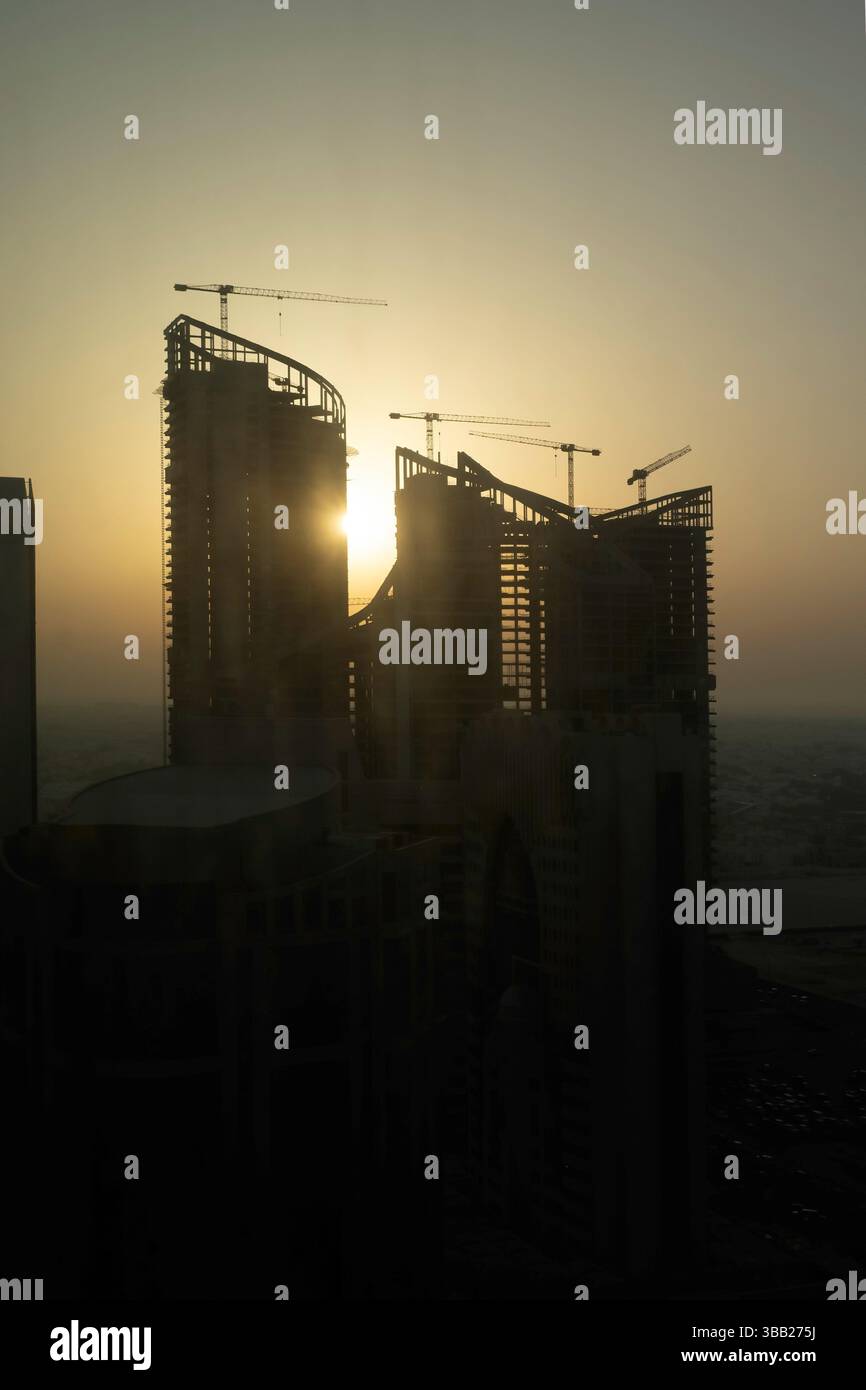 Bau eines neuen Gebäudes. Viele Hochhauskrane und industrielle Baumaschinen gegen die Sonne. Silhouettenkrane Gebäude Stockfoto