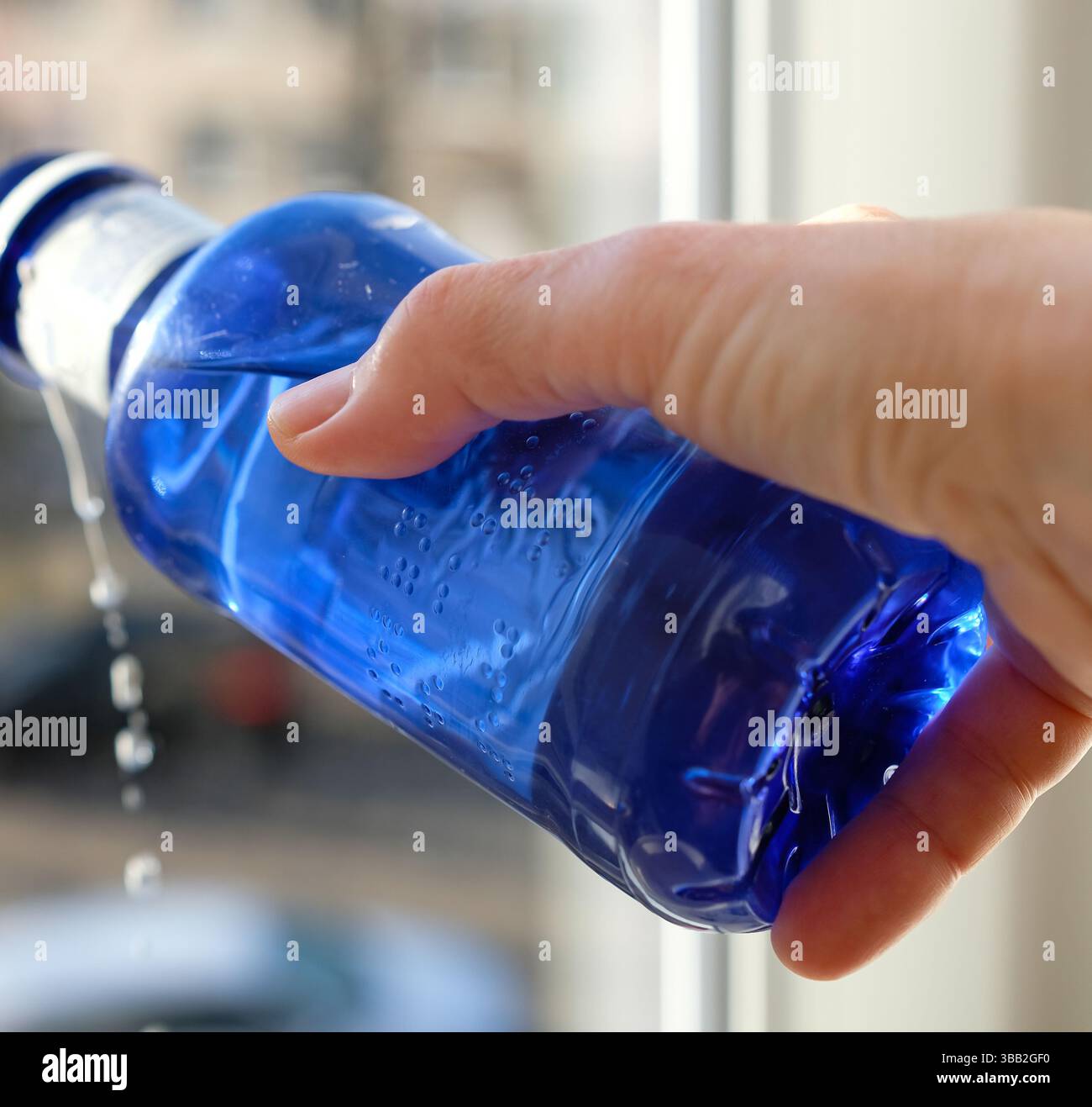 Frau, die Wasser aus einer blauen Flasche gießt. Schrift in BRAILLE-SCHRIFT auf einer Plastikflasche. Erhöhte Punkte. Lesen Sie mit den Fingern. Brailleschrift für Kunststoffverpackungen. Stockfoto