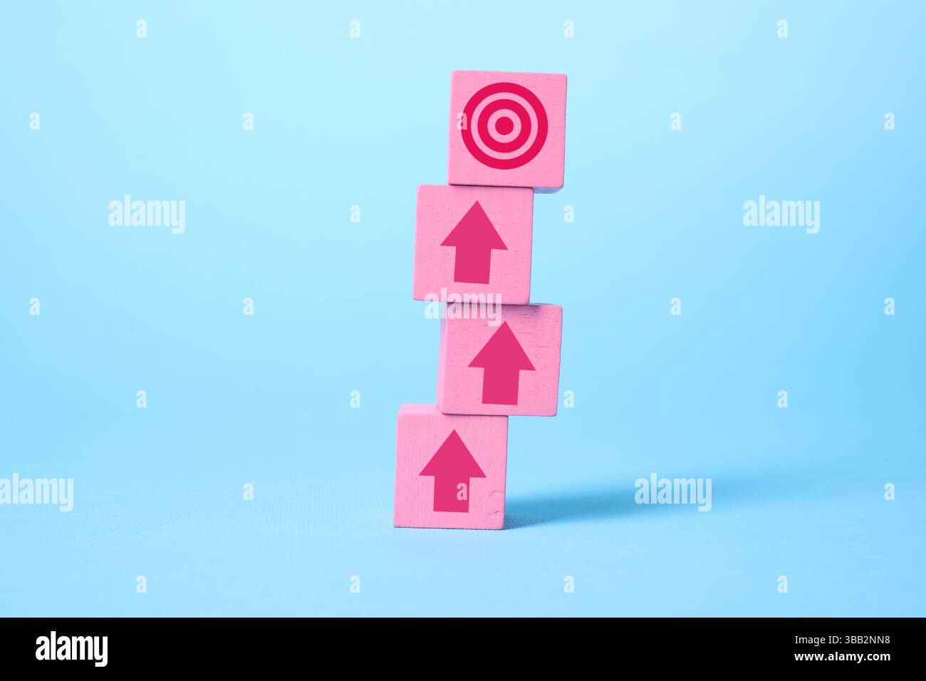 Targeting. Gestapelte rosafarbene Würfel mit Pfeilen auf Bullseye auf dem oberen Würfel vor hellblauem Hintergrund Stockfoto