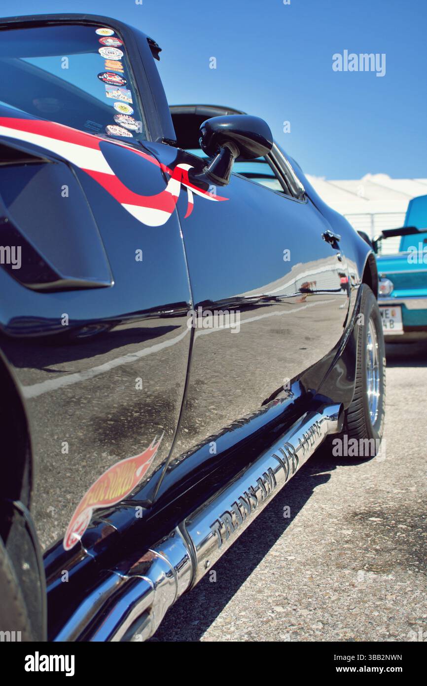 Nahaufnahme des glänzenden seitlichen Auspuffrohrs und des Aufklebers Hot Wheels auf dem schwarzen Custom Car, das die Umgebung reflektiert Stockfoto