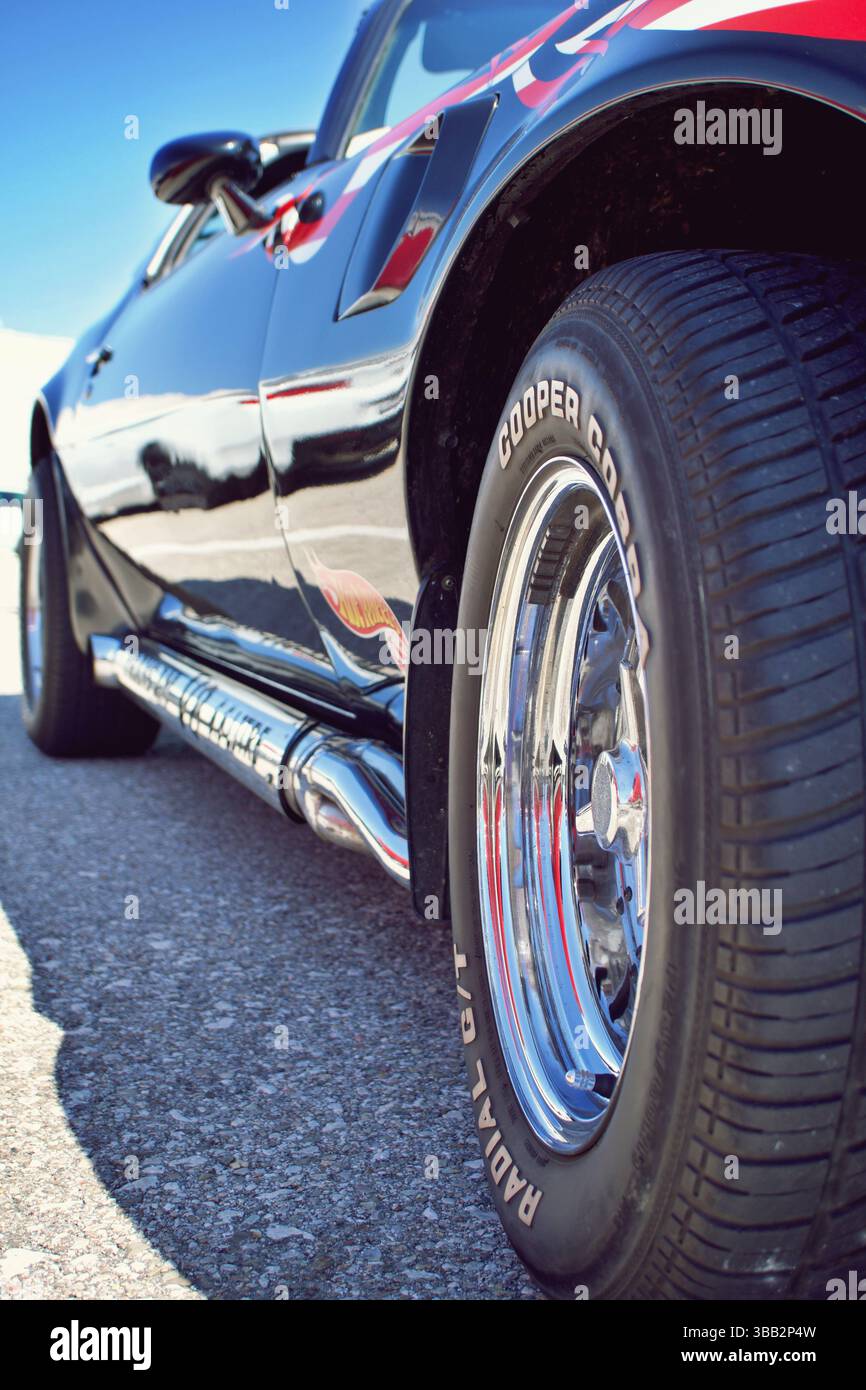 Nahaufnahme des glänzenden seitlichen Auspuffrohrs und des Aufklebers Hot Wheels auf dem schwarzen Custom Car, das die Umgebung reflektiert Stockfoto