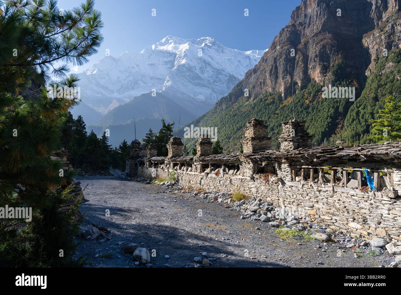 Traditionelle buddhistische Mani-Mauer auf dem Annapurna Circuit zwischen Upper Pisang und Manang, Nepal, mit schneebedeckter Annapurna II hinter Hügeln Stockfoto