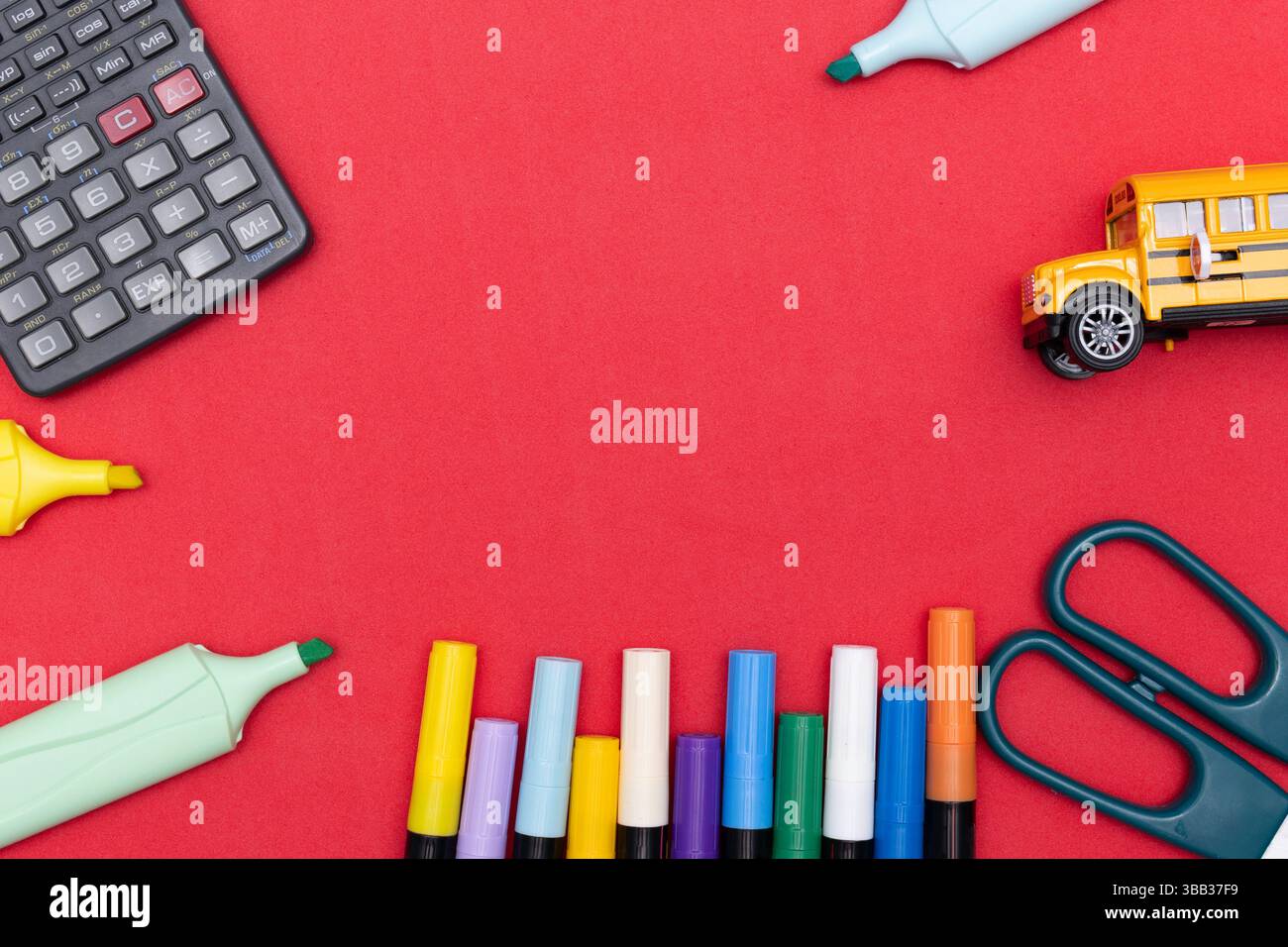 Schulpapier mit farbigen Markierungen, Textmarkern, Scheren, einem Taschenrechner und einem Spielzeugschulbus, der um einen roten Hintergrund mit zentralem C angeordnet ist Stockfoto