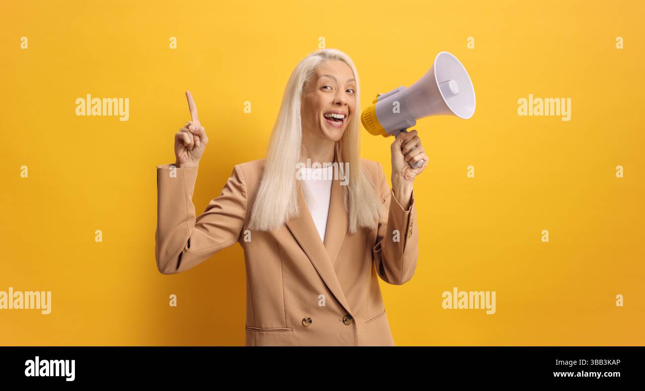 Frau, die mit einem Megaphon spricht und mit dem Finger auf gelben Hintergrund zeigt Stockfoto