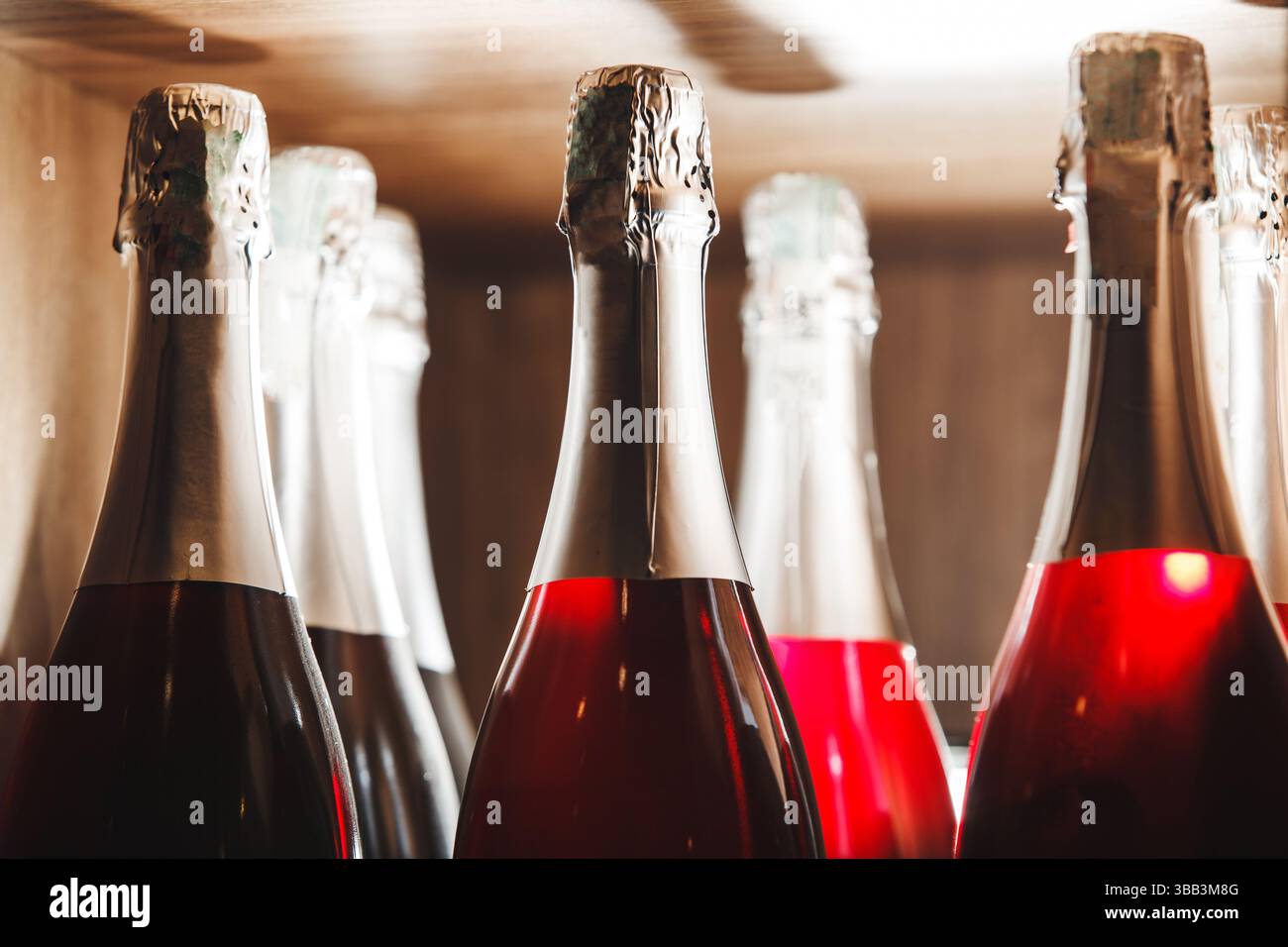 Nahaufnahme von Sektflaschen mit Rosenwein auf Holzregal im Umgebungslicht Stockfoto