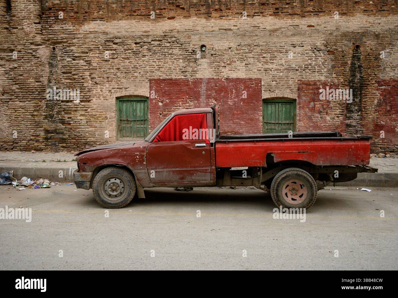 Ein alter roter Pickup-Lkw mit sichtbarem Verschleiß steht neben einer verwitterten Ziegelwand und zeigt eine rustikale und düstere Atmosphäre, die auf vin hindeutet Stockfoto
