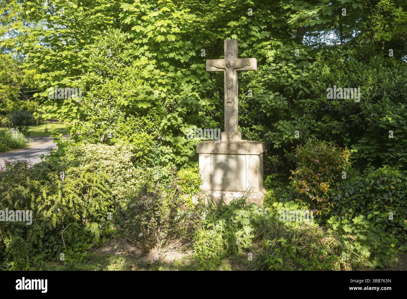 Steinkreuz mit jesus christus Statue in grünen Büschen in der Nähe einer Straße in einem Park, Borken, NRW, Deutschland, Europa Stockfoto