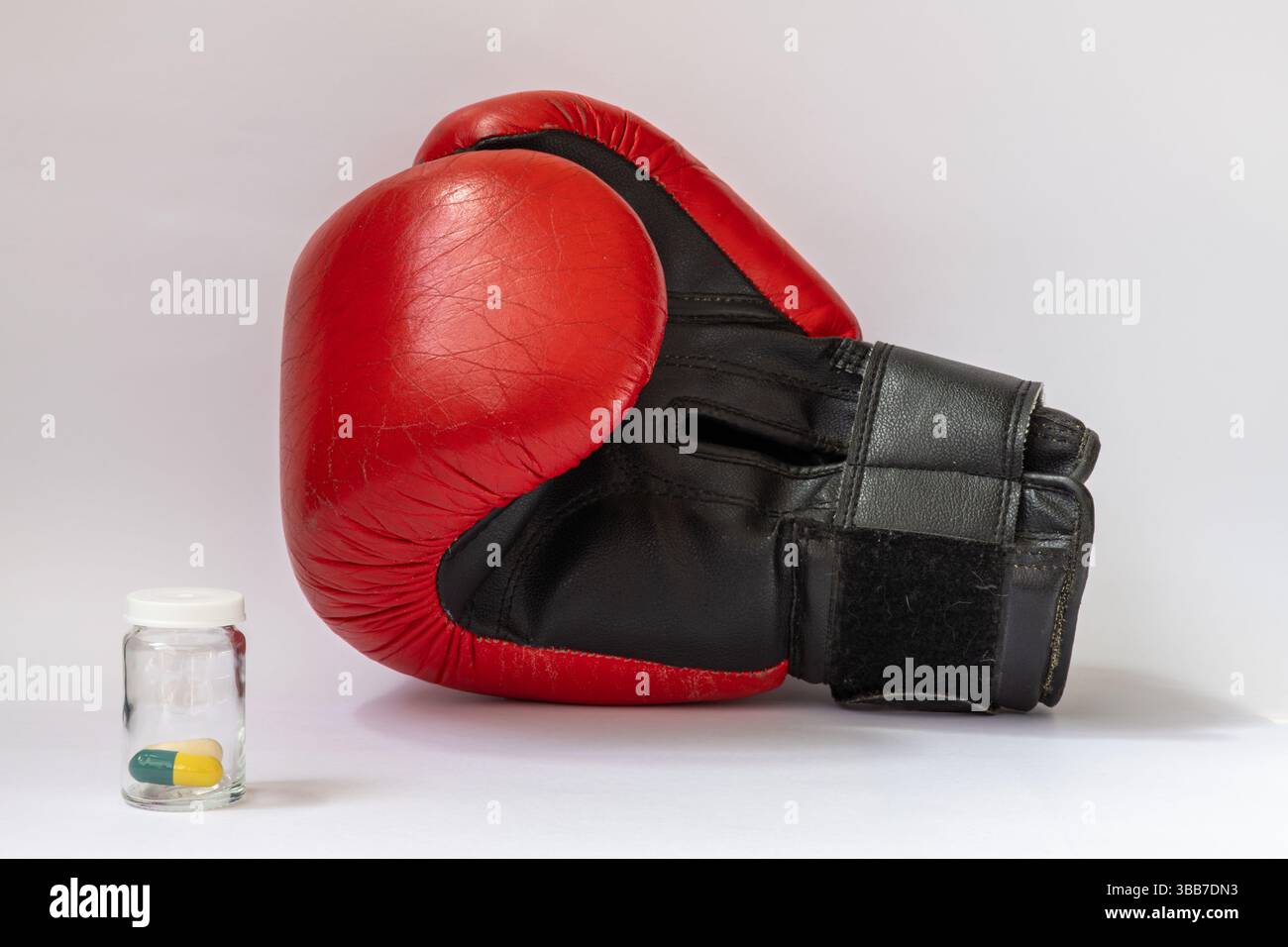 Roter 10 oz Boxhandschuh auf weißem Hintergrund neben Glas jat mit gelb-grünen Pillen Stockfoto