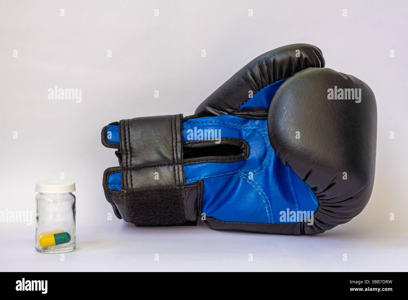 Blauer 8 oz Boxhandschuh auf weißem Hintergrund neben Glas jat mit gelb-grünen Pillen Stockfoto