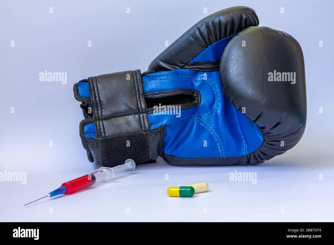 Blauer Boxhandschuh neben der Spritze mit roter Flüssigkeit und gelben und grünen Tabletten auf weißem Hintergrund Stockfoto