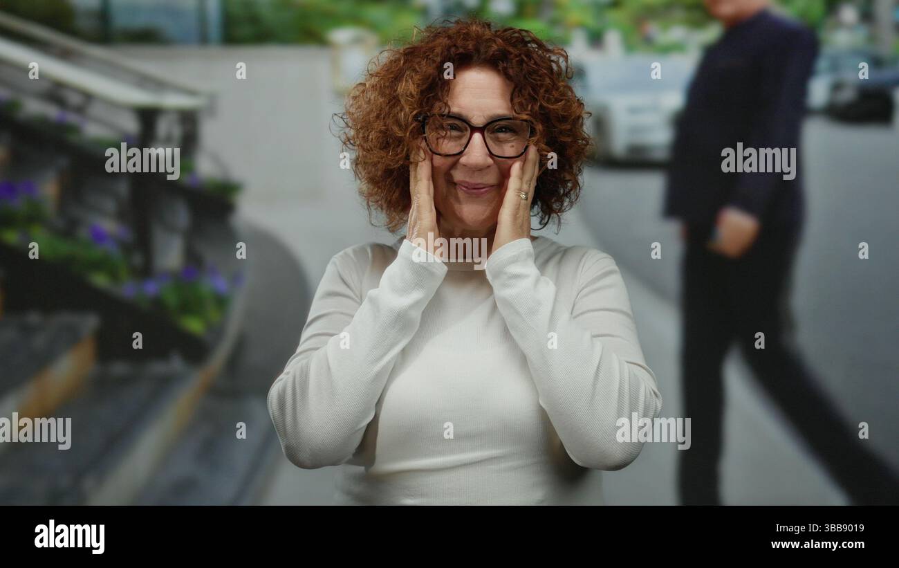 Frau, die auf der belebten Stadtstraße steht, mit ihren Händen im Gesicht Überraschung und Freude ausdrückt, Brille trägt, inmitten eines urbanen Outdoor-Hintergrunds mit ca. Stockfoto