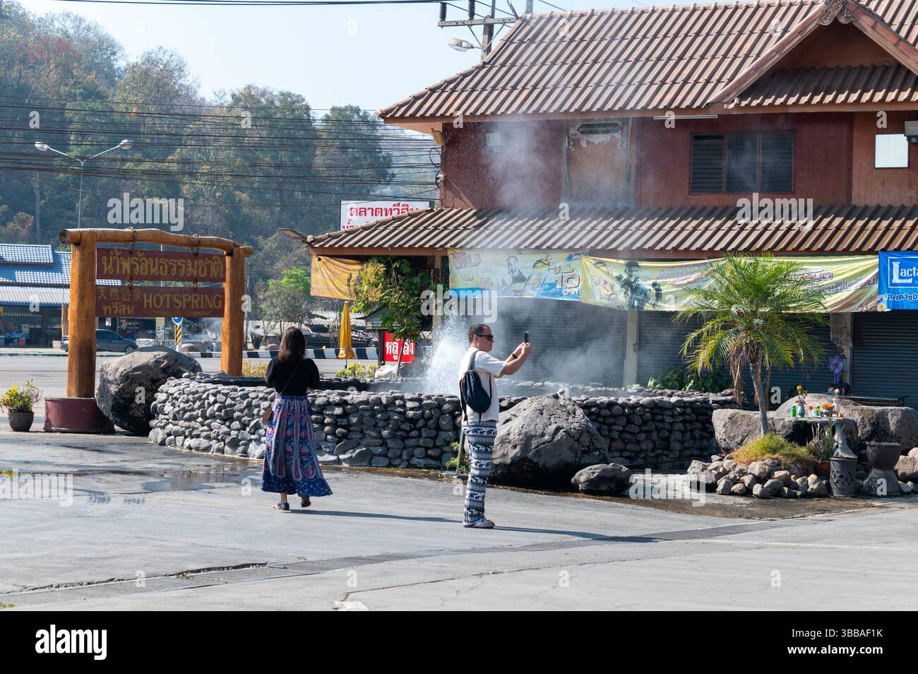 Ein paar Touristen an der sprudelnden heißen Quelle in der Nähe des Haupteingangs der Thaweesin Chiang Rai heißen Quellen, eine beliebte Touristengrube, befindet sich Stockfoto