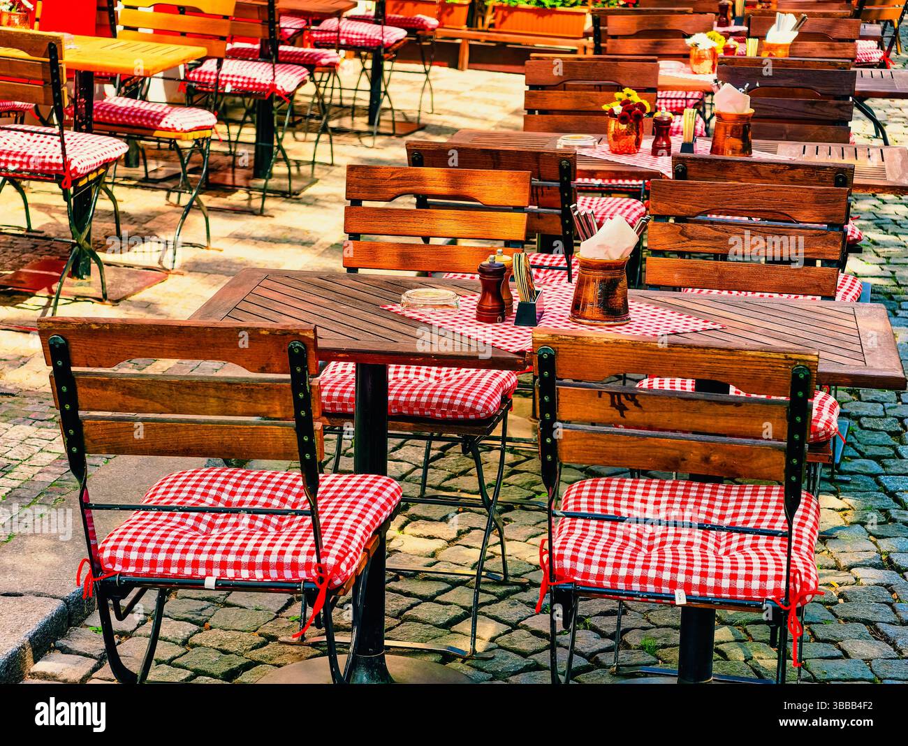 Bezaubernde Terrasse im Freien mit Holztischen und -Stühlen, mit bunten Blumen und üppigem Grün, die eine gemütliche und einladende Atmosphäre schafft, ideal für Entspannung und gesellschaftliche Zusammenkünfte Stockfoto